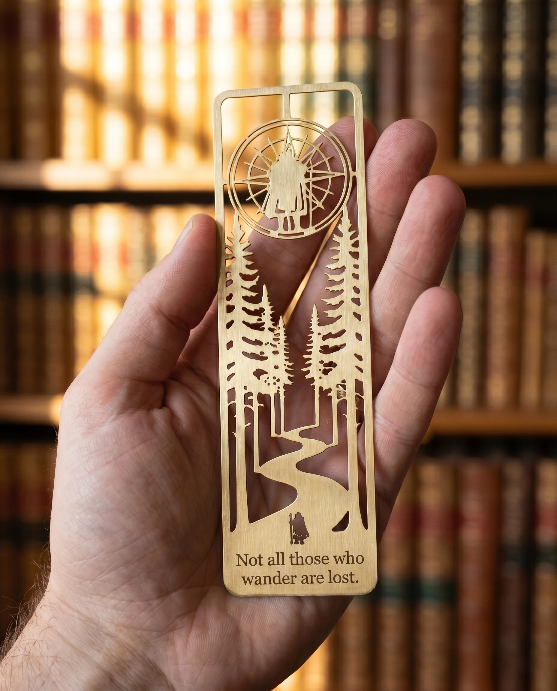 The brass bookmark held flat across an open palm, library shelves blurred in warm background.