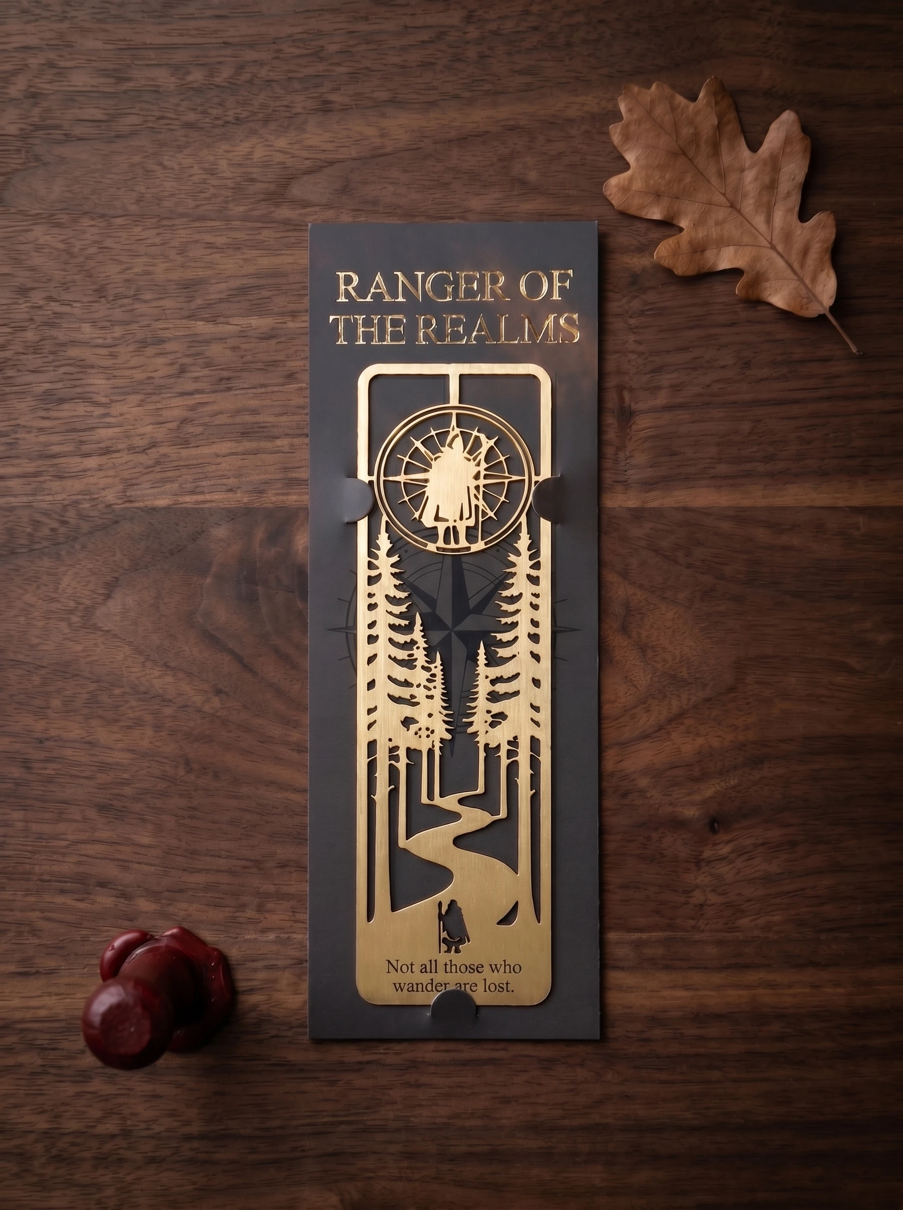 Overhead flat-lay of the brass bookmark on its dark slate presentation card with gold-foil branding, beside a dried oak leaf and red sealing wax.
